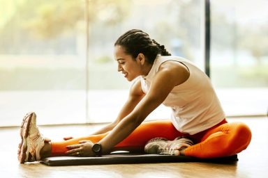 Stretching Femme s'étirant sur un tapis de yoga, vêtue d'un legging orange et d'un haut blanc.